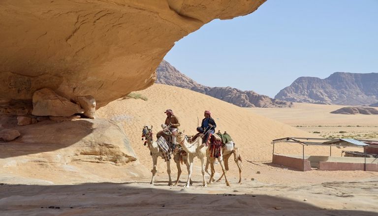 رجال يركبون الجمال عبر الصحراء في وادي رم